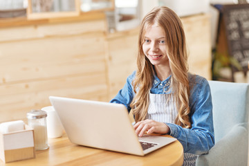 Smiling young lady using laptop in cafe