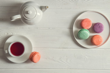 Flat lay. Close up. Provence breakfast. Bright french macarons on a round plate, a cup of berry tea, a teapot. Copy space.