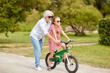 family, leisure and people concept - happy grandmother teaching granddaughter to ride bicycle at...