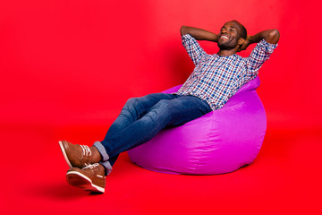 Nice handsome cheerful positive guy wearing checkered shirt sitting on violet purple bag chill out...