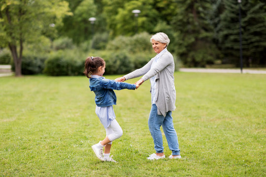 family, leisure and people concept - happy grandmother and granddaughter playing game or dancing at summer park
