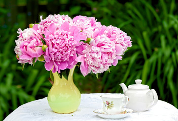 A bunch of pink peonies in a vase in an outdoor setting.