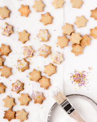 Plätzchen / Kekse gebacken für Weihnachten in Sternform mit Zuckerguss und bunten Streuseln auf weißem Hintergrund von oben bei Tageslicht fotografiert