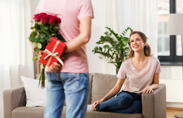 couple, relationships and people concept - happy woman looking at man with flowers and gift at home