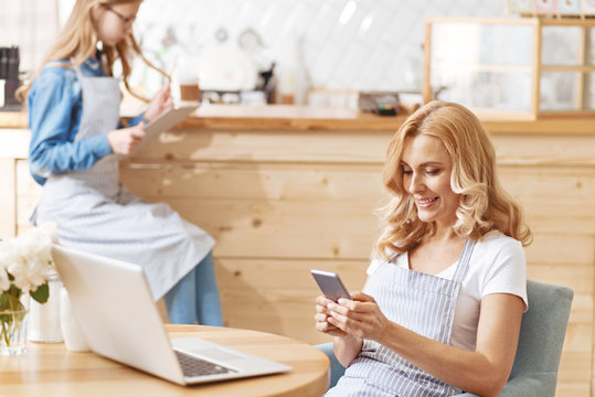 Mature woman wearing apron using smartphone in cafe
