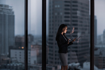 Businesswoman working late using digital tablet with city skyline in background
