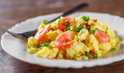 scrambled eggs with shrimp and green onions in white plate on wooden table background.