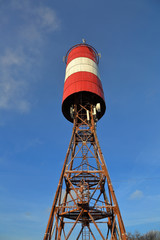 Red and white cell tower on rusty pylons against a blue sky