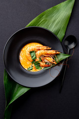 Seafood Soup decorated with whole shrimps and tropical leaves on black plate, black background