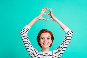 Cropped close up portrait of beautiful cute foxy ginger she her lady fingers hands up above head in figure form of heart gladly smile wearing white striped pullover isolated on teal background