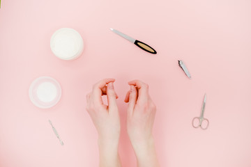 Female hands with white cream jar and manicure kit, scisors, polisher. Skin care concept. Light pink abstract background.