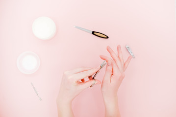 Female hands with white cream jar and manicure kit, scisors, polisher. Skin care concept. Light pink abstract background.