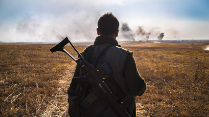 A soldier looks out onto the battlefield with a semi-automatic rifle strapped to his back