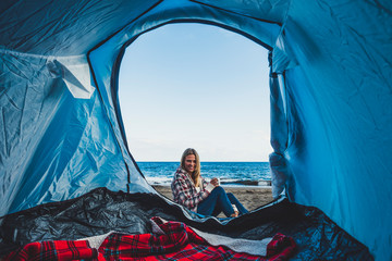 Beautifl cheerful blonde girl smiling viewed from inside a tent camped at the beach directly on the...