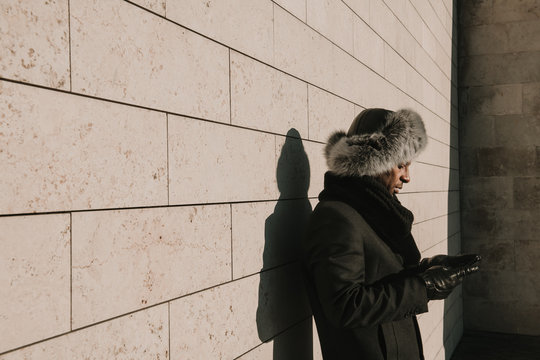 Side view of man using cell phone while leaning on wall