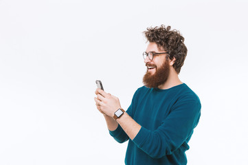 Portrait of cheerful bearded hipster man using smartphone over white background