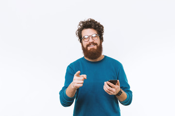 Happy smiling bearded man pointing at the camera and holding smartphone