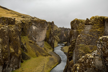 Deep canyon, steep cliffs overgrown with green moss, surrounded by a very fast river with cold water. Canyon of Icelandic tales - Fjardrarglufur