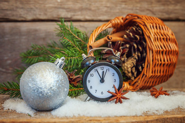 Fototapeta na wymiar Christmas New Year composition winter objects fir branch basket pine cones balls alarm clock on old rustic wooden background. Xmas holiday december decoration copy space. Time for celebration concept