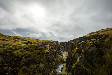Fototapeta na wymiar Deep canyon, steep cliffs overgrown with green moss, surrounded by a very fast river with cold water. Canyon of Icelandic tales - Fjardrarglufur