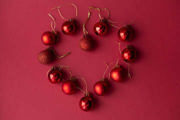 Red Christmas tree decorative toy balls on red celebratory Christmas background laid out in the shape of a heart. New Year's holidays. Christmas holidays