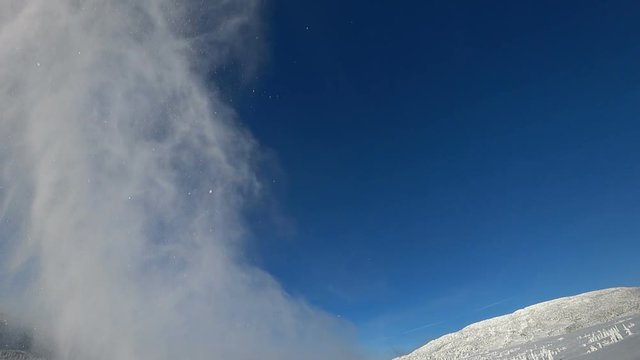 bottom view. the rider on a snowmobile flying with a train of snow whirlwinds. a wave of snow flies beautifully into the camera, against the blue sky in a mountain valley. super slow motion video. hig