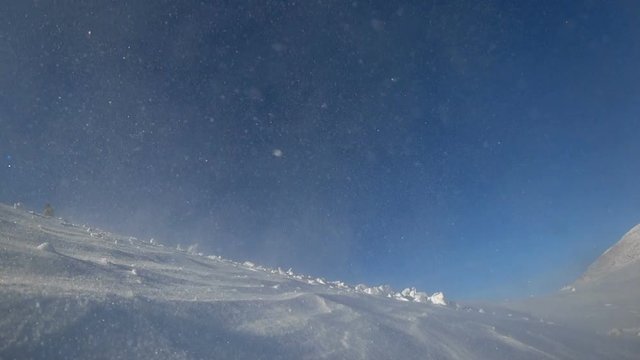 a snowmobile rider jumps into the valley with snow whirlwinds. flying from right to left, a wave of snow from the caterpillar into the camera, against the blue sky in the mountain valley. high quality