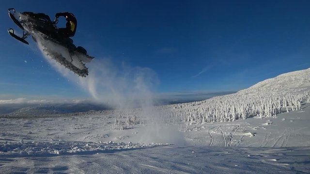 guy on a snowmobile jumping and flying high. from right to left, against a blue sky and a beautiful snow-covered mountain valley. super slow motion video. high quality