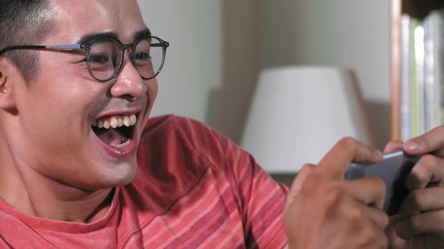 Close up of young Asian man holding smartphone in hands, typing and laughing because of received message