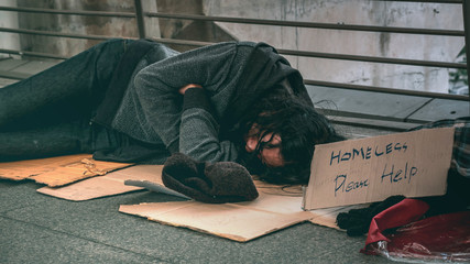 Poor homeless man or refugee sleeping on the dirty floor of the public path way in the city.