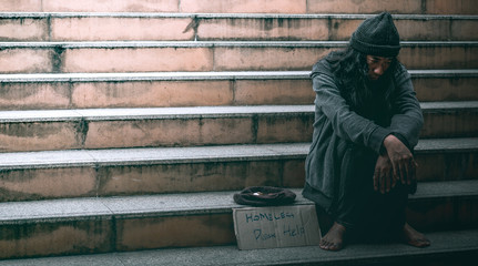 Poor homeless man or refugee sitting on the stairs at urban street in the city begging for money.