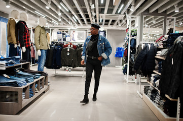 Stylish casual african american man at jeans jacket and black beret with fanny pack or waist bag walking at clothes store.