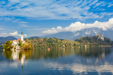 Fototapeta na wymiar Lake Bled, Slovenia. View at Church of the Assumption of Maria. Bled castle at the background. Cloudy sky