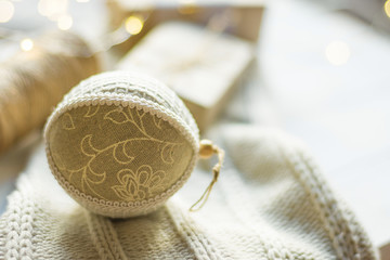 Fototapeta na wymiar Christmas New Year presents packaging. Gift boxes in craft paper tied with twine hand made linen fabric ball knitted sweater on wood table by window. Golden garland bokeh lights. Cozy winter evening