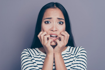 Close-up portrait of attractive scared straight-haired lady in striped pullover blouse biting nails...