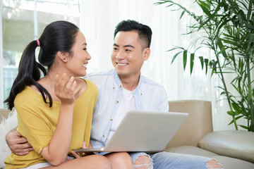 Obraz premium Beautiful casual ethnic couple sitting on couch with laptop spending time at home in leisure