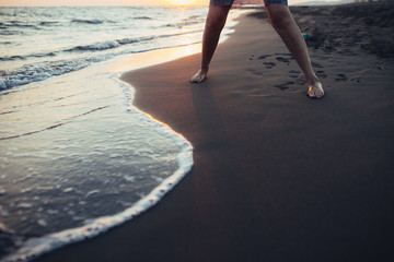 Young woman walking by the sea at the sand beach on a sunset