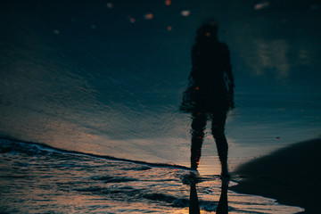 Reflection in the sea water of a young woman standing and looking to the sea