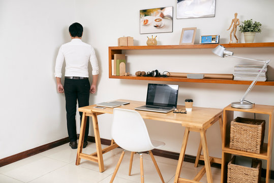 Rear view of businessman standing in the corner of room near his workplace at office, he's guilty of his work