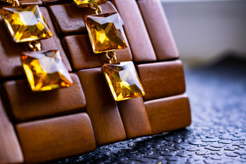 Beautiful and fashionable jewelry and accessories for women. Yellow, orange stones with square stones on dark and wood textured background. Mustard bright rhinestones on a Gold metal base. Interesting