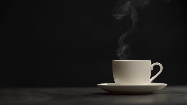 Steaming coffee cup on black background. Puffs of steam slowly coming from a white cup of hottest coffee. Slow motion shot