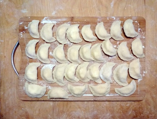 dumplings on a wooden board in flour. top view. raw frozen. traditional meal.