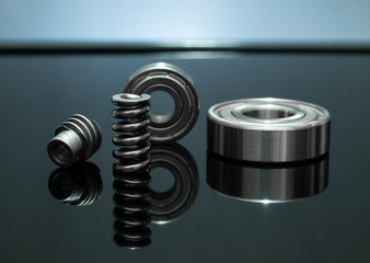 Close up view. Spare parts is spring with bearing and cog are small placed on black glass floor. There is reflection with background as backlight.