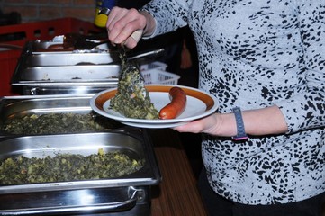 Personen servieren Grünkohl und Mettwurst an einem Buffet