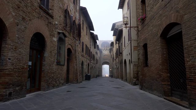San Gimignano, Italy. Walking a narrow street of the Medieval town, filled with the aura of old times. There are old brick-walled buildings on both sides of the street. 4K