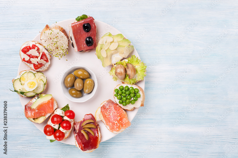 Poster Different kinds canapes in plate on the blue wooden background.