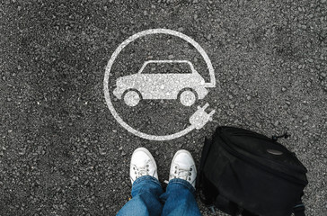 a man with a shoes is standing next to electric car sign on road asphalt - obrazy, fototapety, plakaty