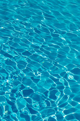 Blue water in swimming pool background. Ripple Water in swimming pool with sun reflection. Blue swimming pool rippled water detail. vertical photo