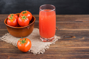 Tomato juice with tomatoes on black and wooden background.