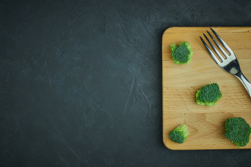 Obraz na płótnie Canvas placer of broccoli green cabbage on a cutting board with a fork. Template of healthy food on a dark background. Copy space Top view. Vegetarian food. syroedenie.